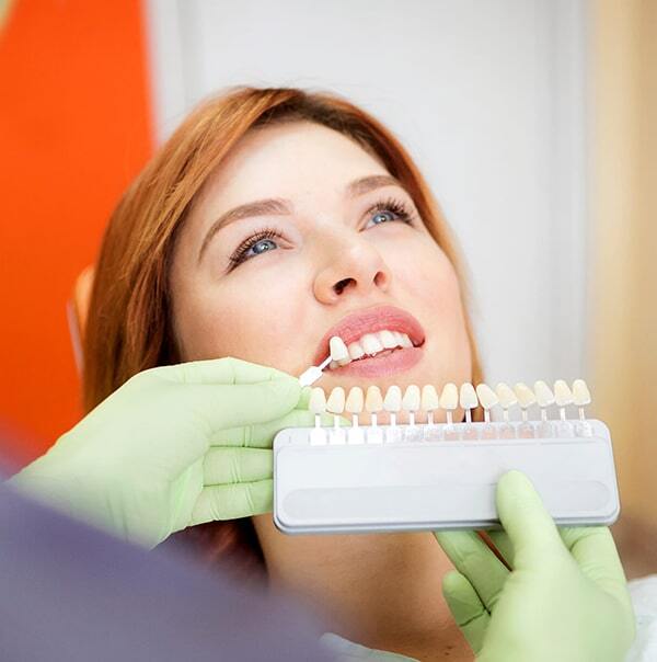 Dental professional holding tooth shade guide against patient's teeth during color matching consultation.