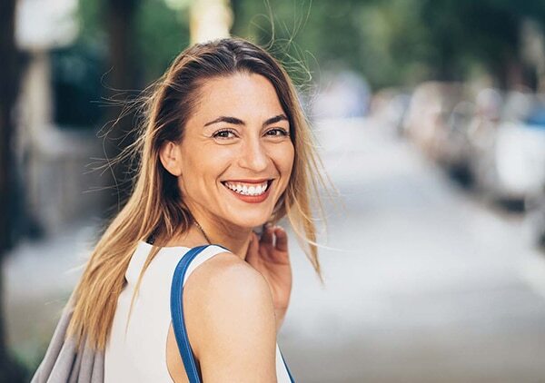 Young woman smiling at camera outdoors on urban street during daytime.