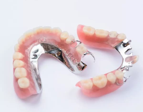 Partial dentures with pink acrylic base and artificial teeth displayed on white background.