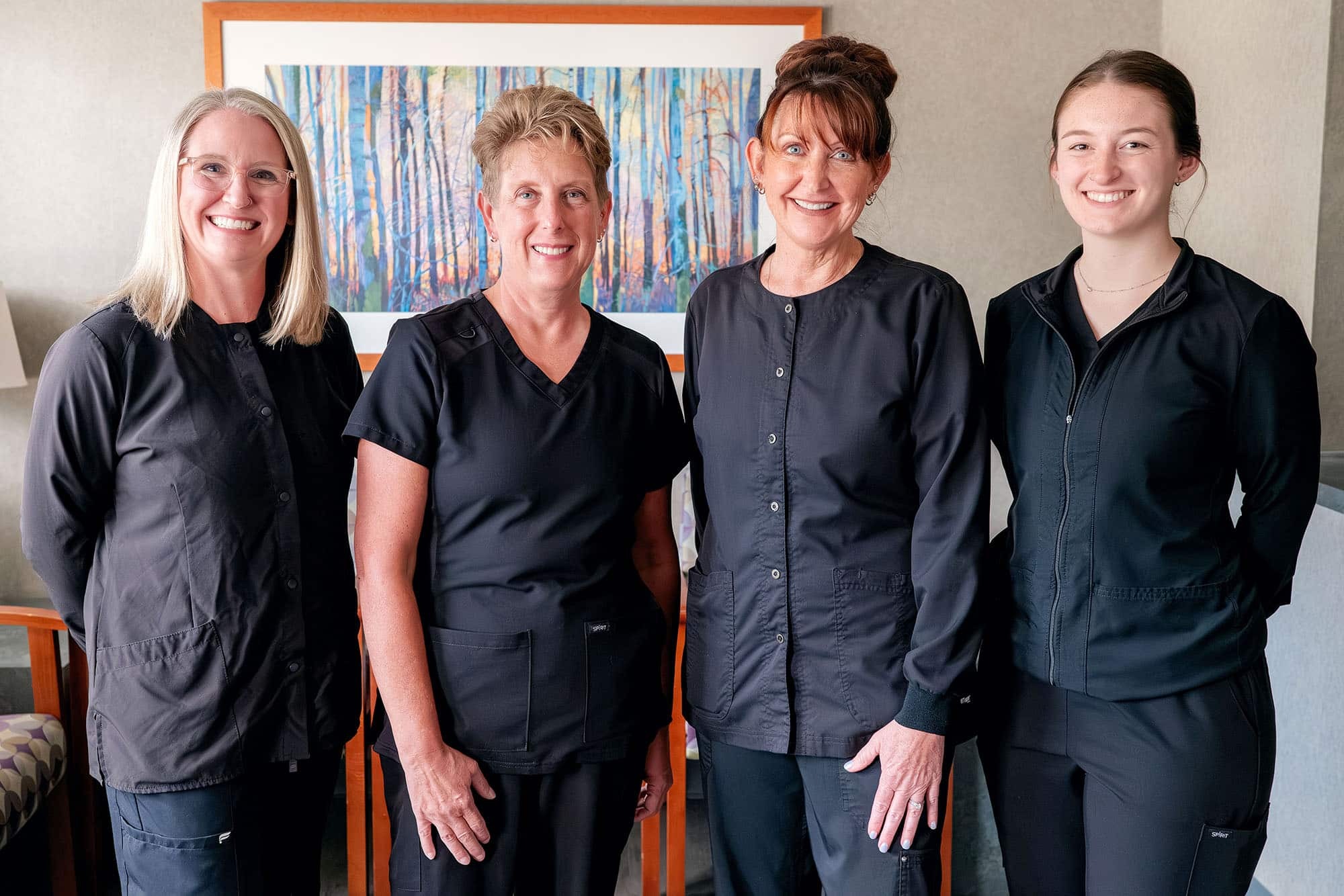 Four dental professionals in dark uniforms standing together in a clinical office setting.