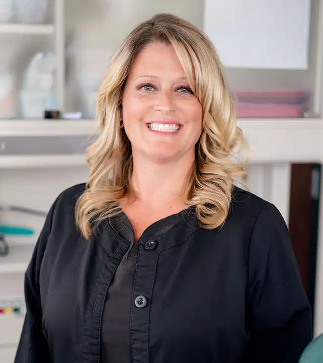 Professional woman smiling at camera in modern dental office setting wearing black shirt.
