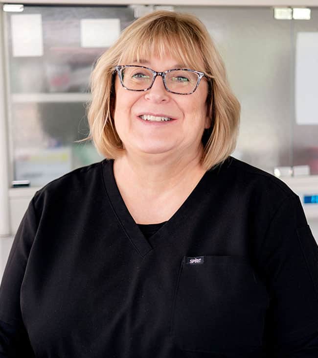 Woman wearing glasses and black shirt smiling at camera in dental office setting.