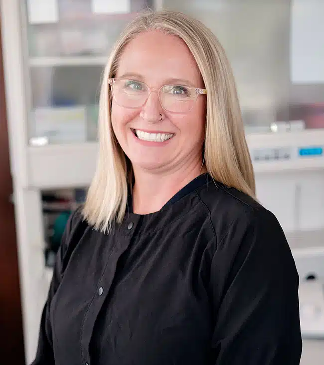 Professional woman wearing glasses and black shirt smiling in dental office setting.