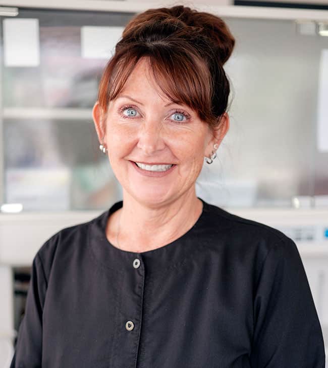Professional woman smiling at camera in modern dental office setting, wearing black cardigan.