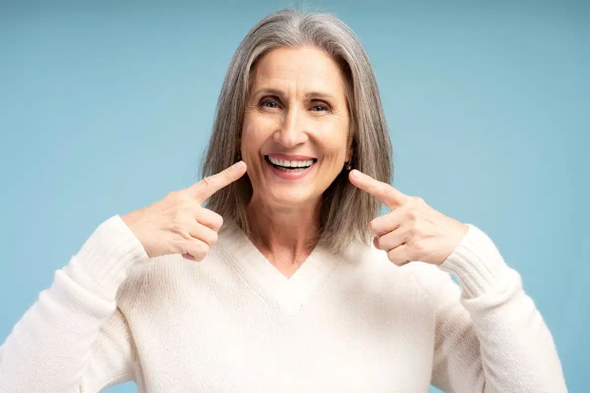 Smiling older woman pointing to her teeth, highlighting improved confidence and oral function after dental implant treatment.
