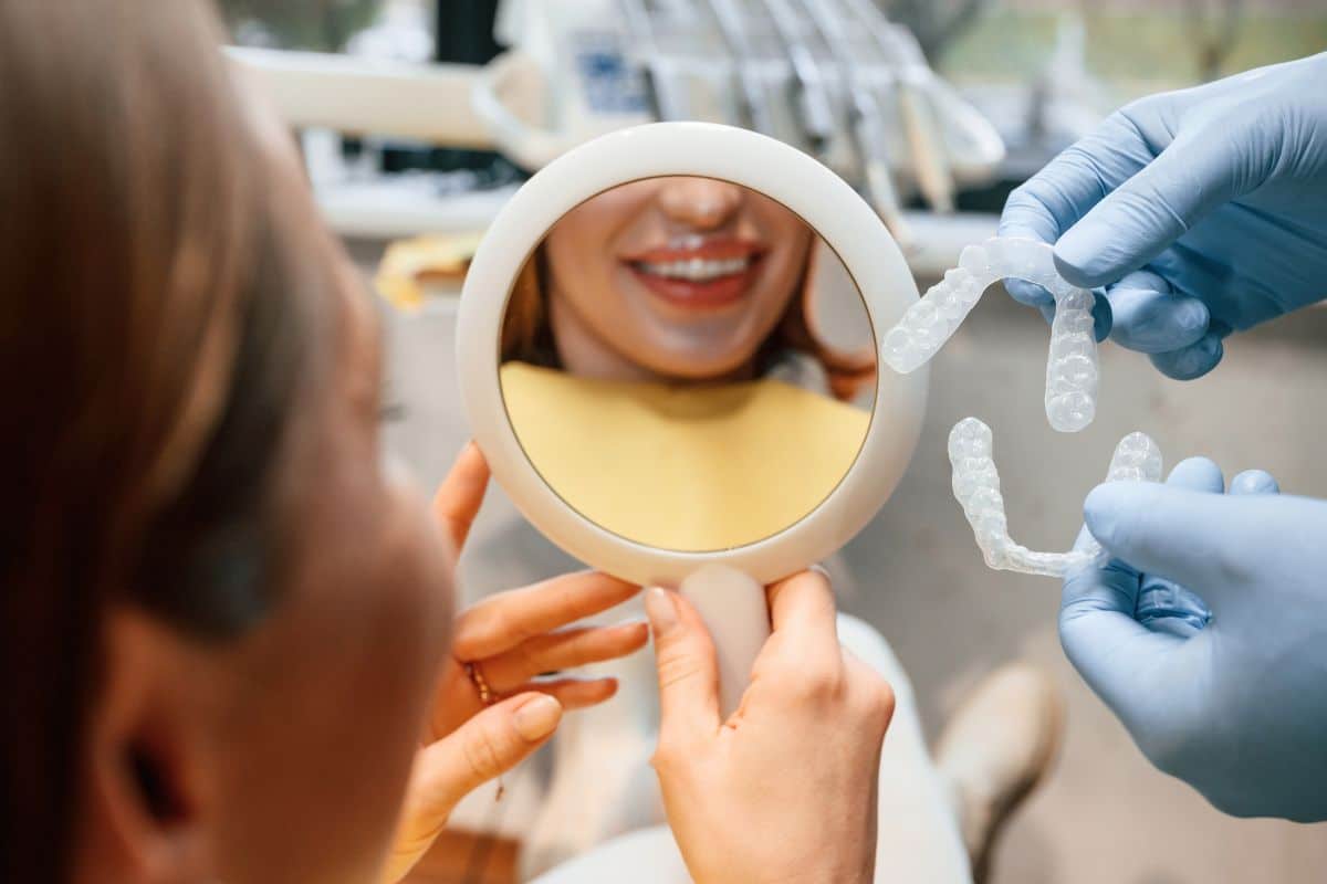Dentist showing clear aligners to a patient using a dental mirror